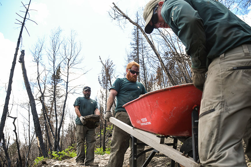 Trail crew members remove rocks from a wheelbarrow