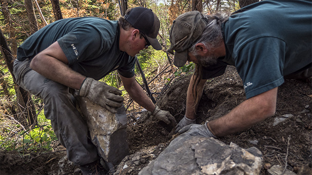 Two workers are digging in the soil to prepare for the construction of a new retaining wall on the trail.