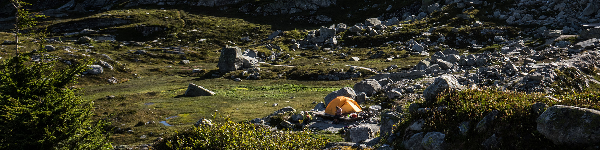 Orange tent on a tent pad on a rocky meadow