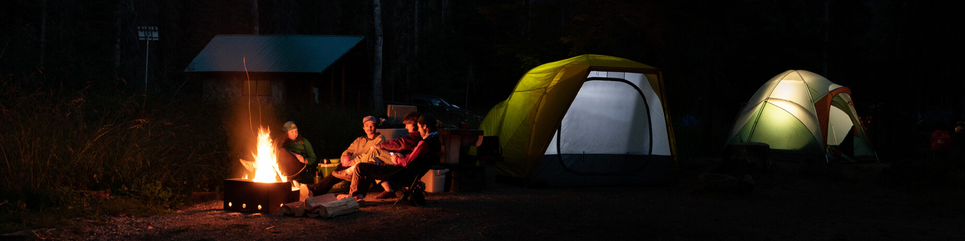 Four people in front of a fire in a campsite