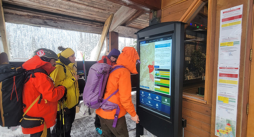 Four people looking at a digital kiosk displaying the avalanche bulletin