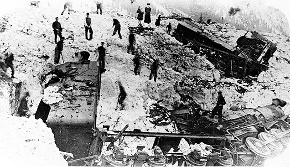 Derailed locomotive and rail cars on their sides, stuck in avalanche debris, as railworkers dig them out.