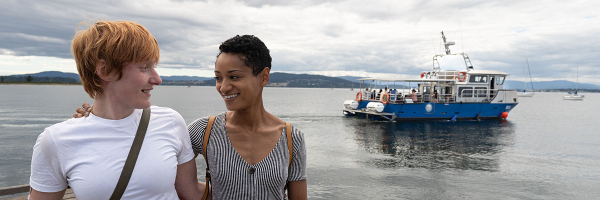  Two people are hugging and looking at each other, and the blue Sidney Spit Ferry is in the background.