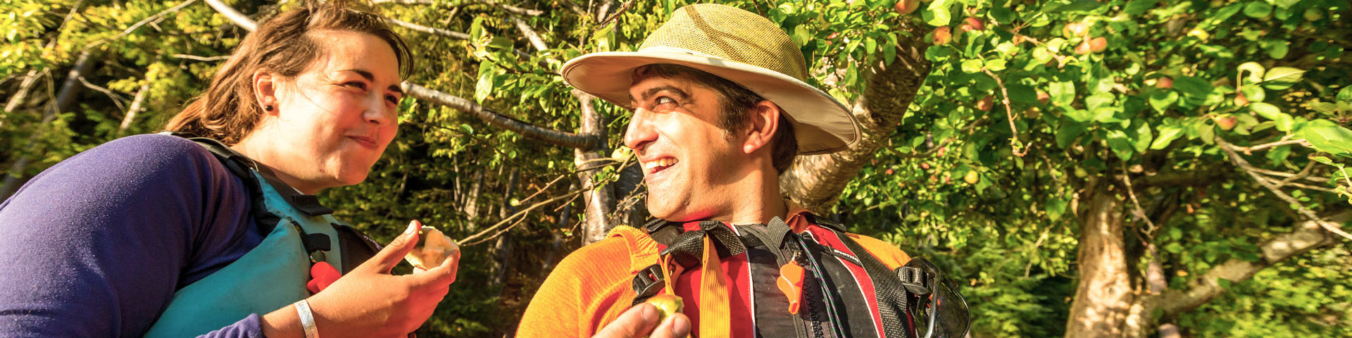 A woman and a man happily eat apples under an apple tree at Shingle Bay, North Pender Island.
