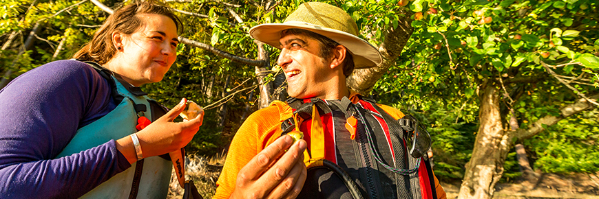 A woman and a man happily eat apples under an apple tree at Shingle Bay, North Pender Island.