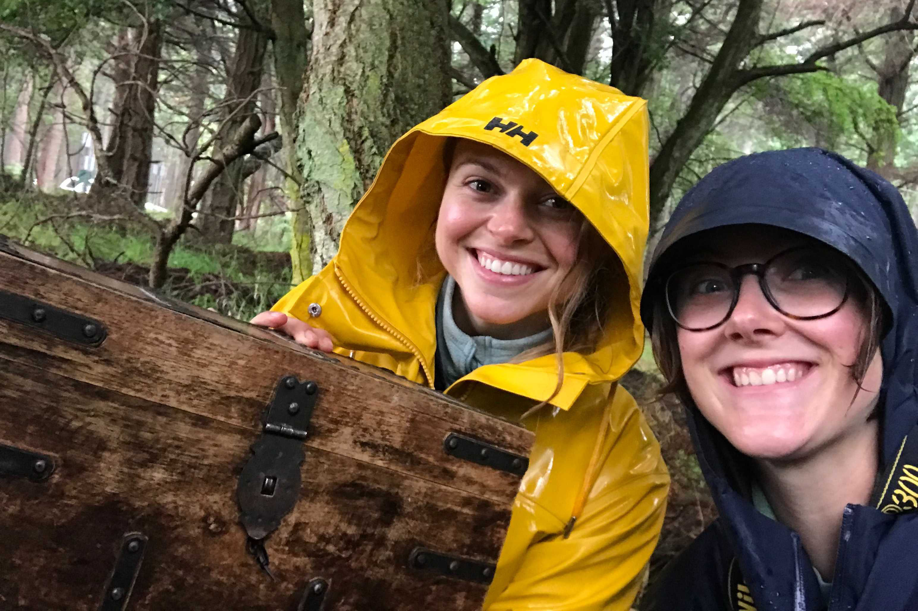 Two people hold a chest made out of wood in the rain. 