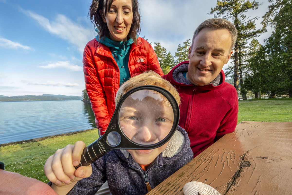 Family looks through a magnifying glass next to ocean.