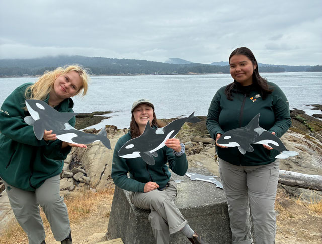 A group of people holding orca cutouts.