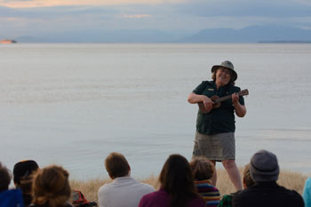 Interpreter strums musical instrument next to ocean.