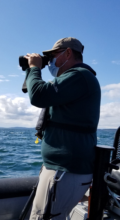 Un chercheur de Parcs Canada, debout dans un bateau sur l’océan, guette la présence d’épaulards résidents du Sud dans l’eau à l’aide de jumelles.