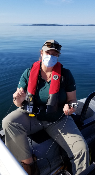 Un écologiste de Parcs Canada portant un masque sourit à la caméra tout en tenant un hydrophone portable immergé dans l’océan.