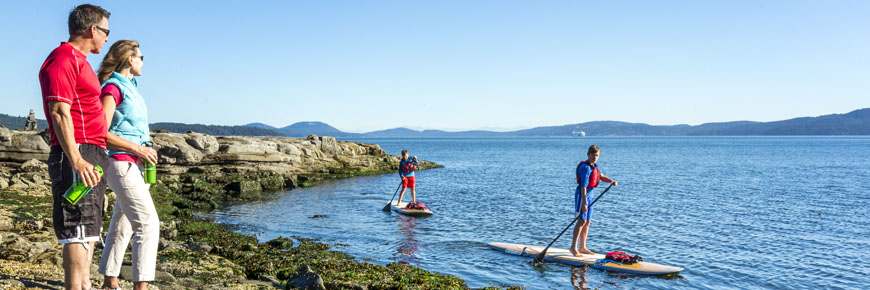 A couple watch some Stand-Up Paddleboarders pass nearby Arbutus Point, on Princess Margaret (Portland Island).