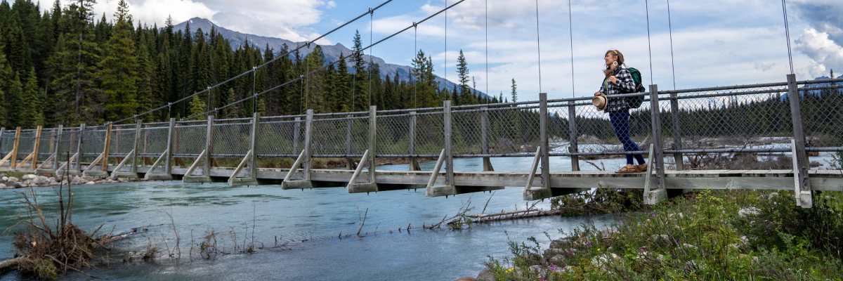A hiker stands on a suspension bridge over Kootenay River enjoying the view