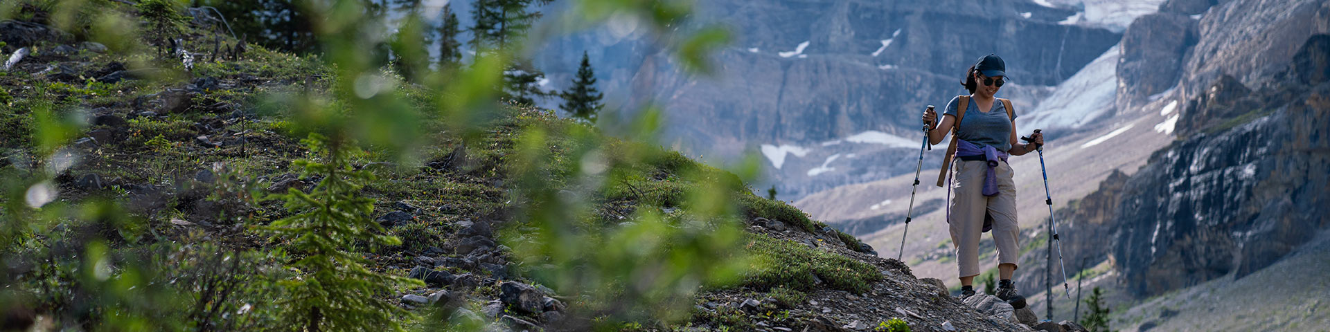 Un randonneur avec des bâtons en descente avec des montagnes et des glaciers en arrière-plan.