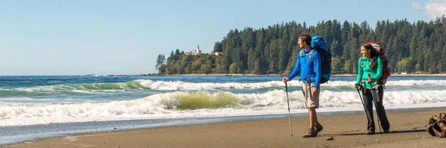 Two hikers walk along a beach. 