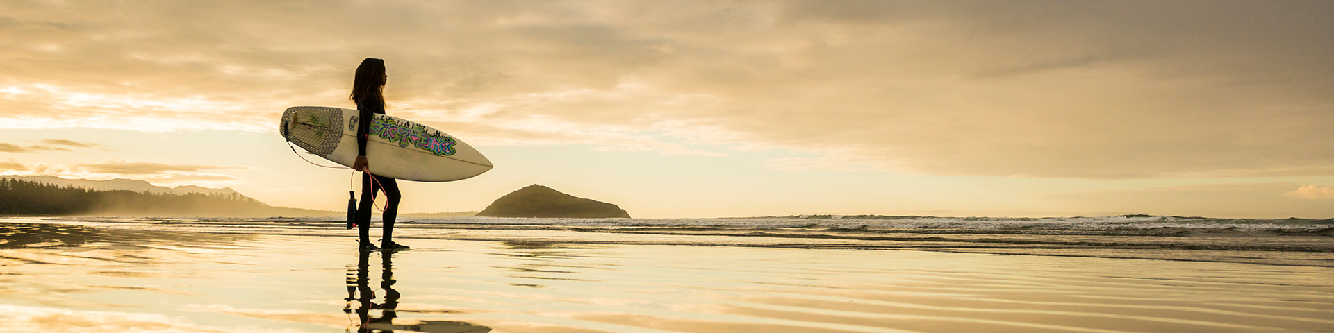 Surfer with surfboard silhouetted in the back drop of the beach