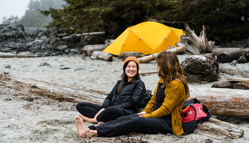 Two people sitting on the beach with a tent in the background