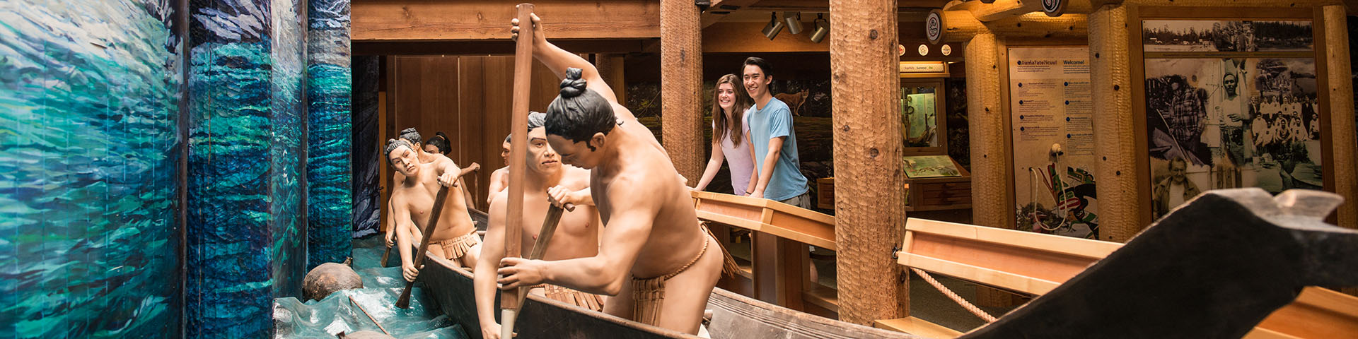 two people looking at a replica of a whaling canoe with whalers inside