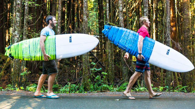 Two surfers with surfboards walking down forested road.