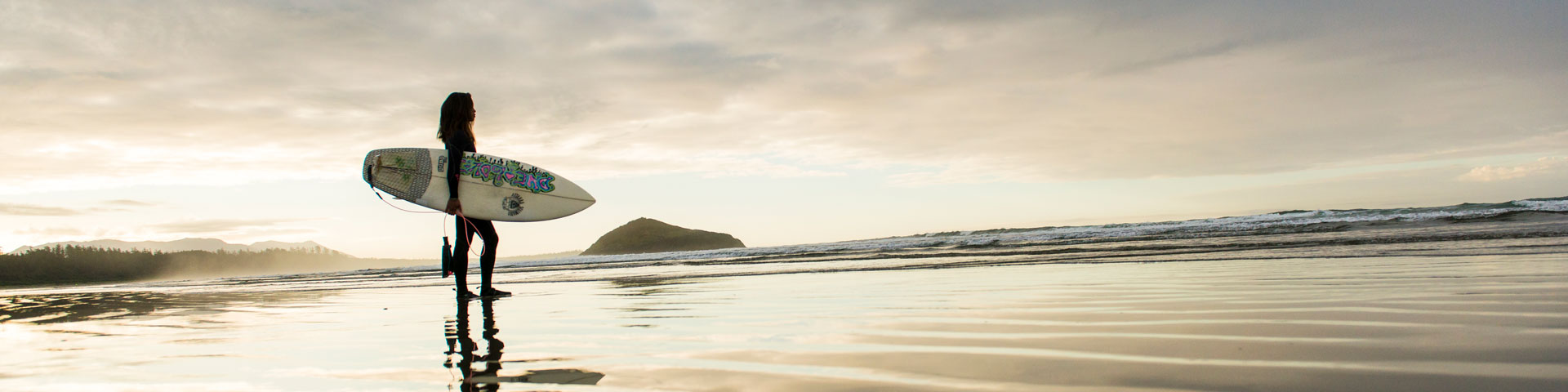 Surfer with surfboard silhouetted in the back drop of the beach.