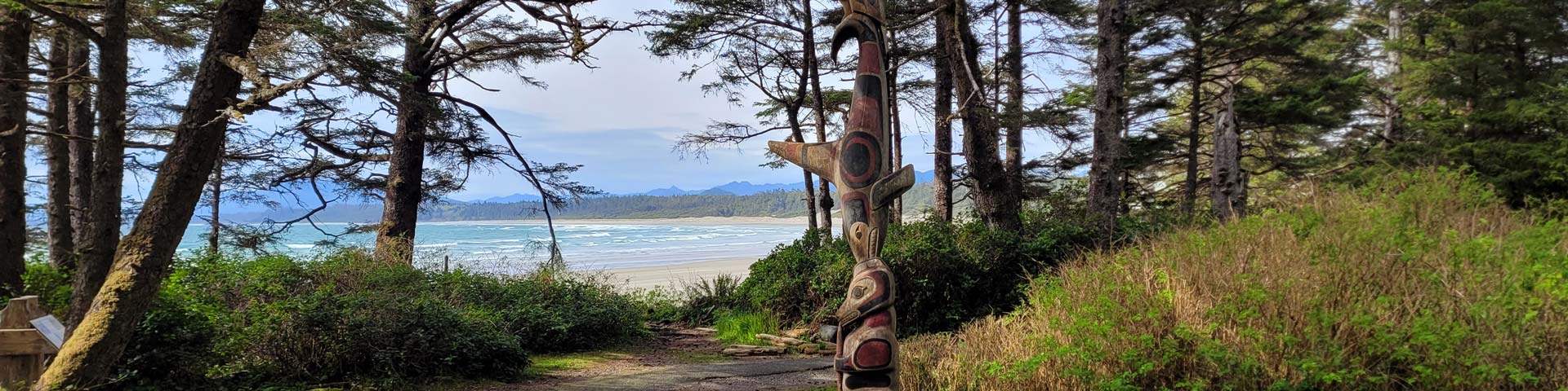 Looking through the trees at a beach with a totem pole in the foreground