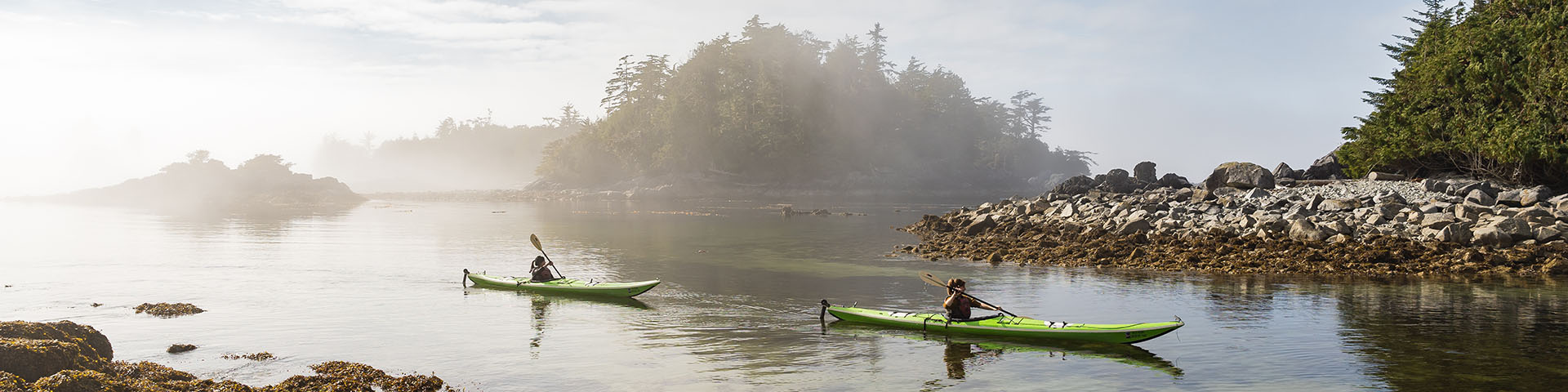 Two kayakers paddling through a channel of clear sea water