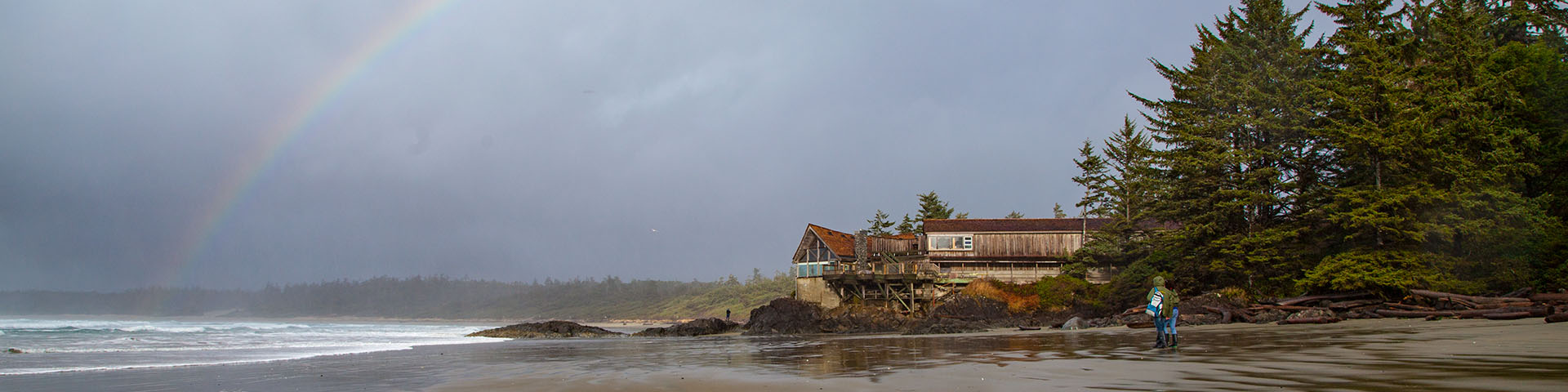 Beach with a wooden building on shore and a rainbow in sky