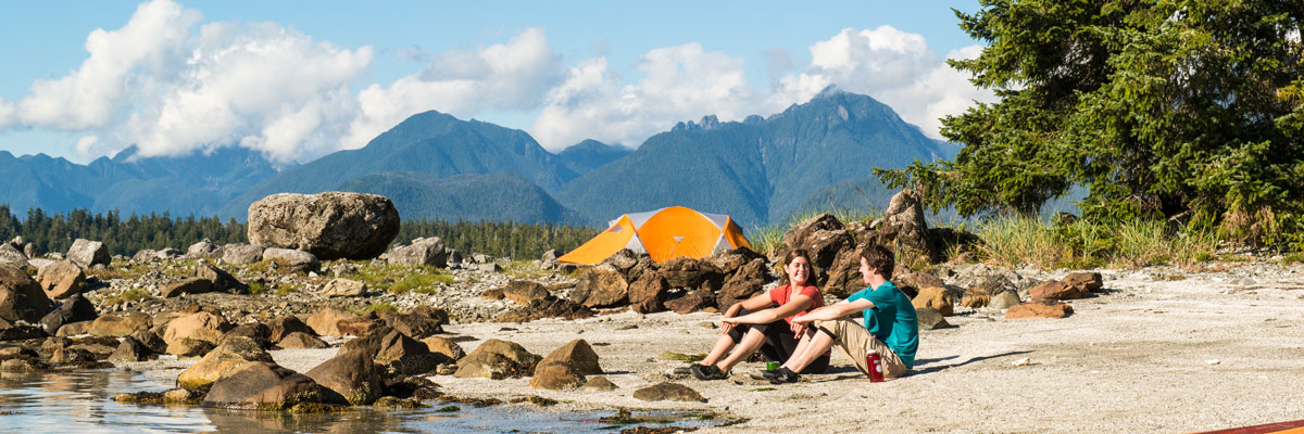 two people sitting on beach in Broken Group Islands with kayak and tent.