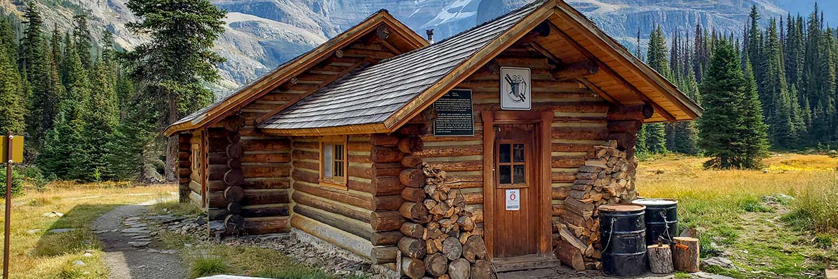 The Elizabeth Parker hut sits in an open meadow with mountains towering behind it.