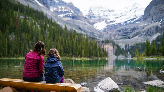 A woman and child sit on a bench at the shore of Lake O’Hara