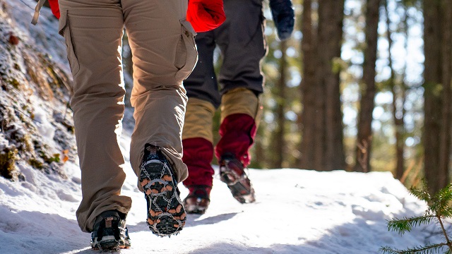 Two people wearing ice cleats walk on a snowy trail.