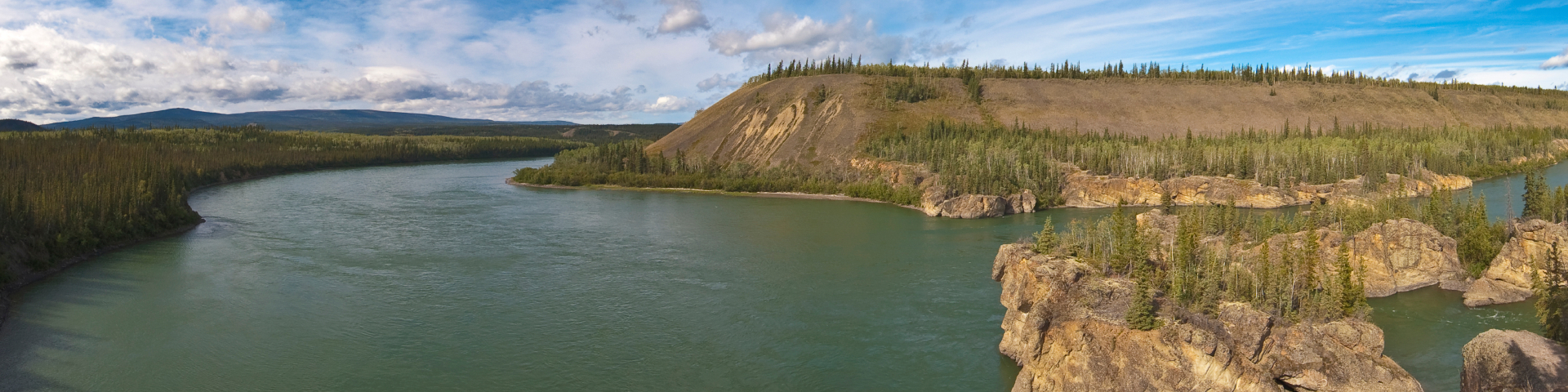 Teetł’it Gwinjik (Peel River) with rocky islands and low-lying forests on a sunny day. 