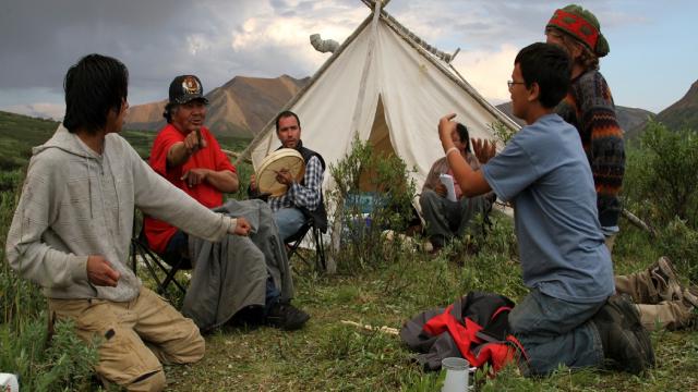 Group of people sitting in a circle on the ground playing hand games.