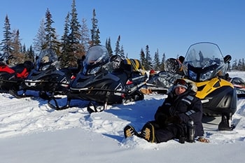 A Parks Canada employee sits in the snow leaning against the back of a snowmobile.