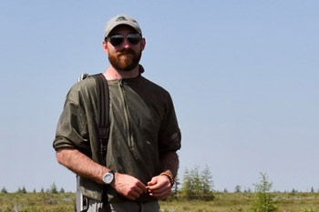 A Parks Canada employee wearing sunglasses looks at the camera while in an open grassy area.