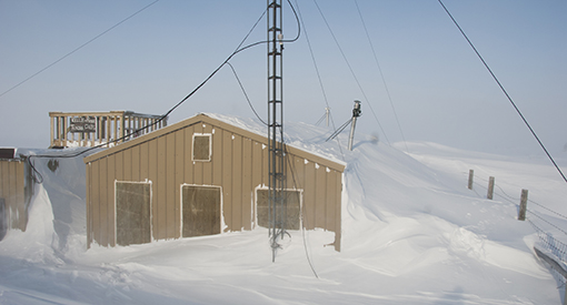 A house surrounded by snow. The doorway is partially blocked by snow.