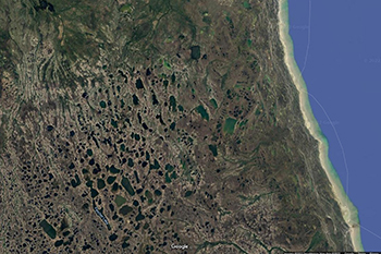 A satellite view of a forested section of land with small bodies of water. To the right of the image is a coastline with water.