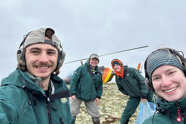 Quatre employés de Parcs Canada posent pour une photo devant un hélicoptère dans le parc national Wapusk.
