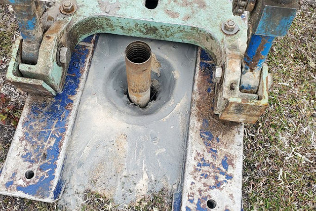 Le tube métallique dans le sol est entouré de la base bleue de la foreuse.