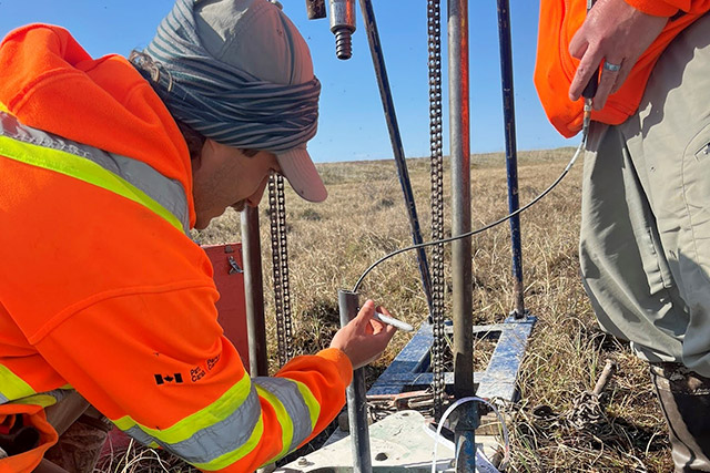 Un employé de Parcs Canada en uniforme insère un tube métallique dans le sol.