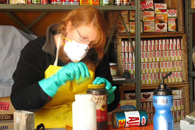 A person wearing a mask and rubber gloves cleans off an artifact in a lab.