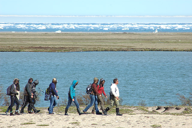 Des personnes marchent sur le sable avec en arrière-plan, une étendue d'eau et des petits icebergs.