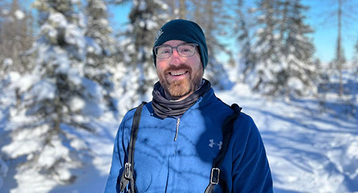 A Parks Canada employee wearing winter clothing smiles at the camera in a snowy forest.