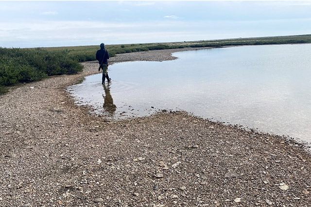 Une personne entre dans un plan d’eau. Il y a un rivage rocheux à l’avant et à gauche de l’image.