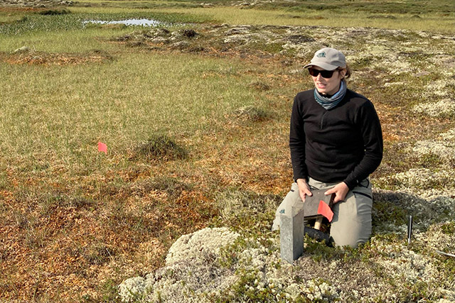 Une personne s’agenouille dans un champ en tenant un bloc-notes.