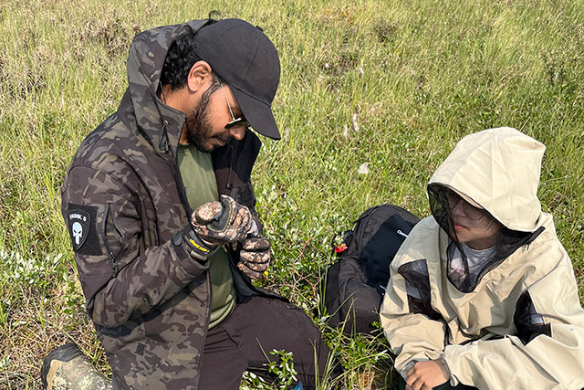 Une personne agenouillée dans un champ tient un petit appareil pendant qu’une seconde personne observe.