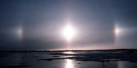 A bright light in the sky in the centre of the image with two smaller bursts of light to the left and right above ponds on the ground.