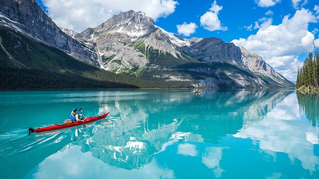 kayaker on blue lake with mountains reflecting in the water