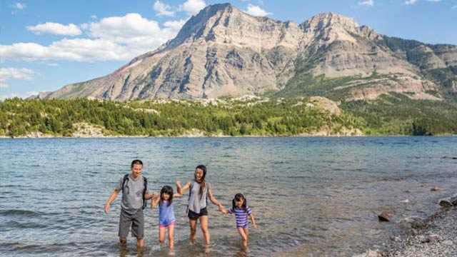 A family wading into a lake with mountains behind