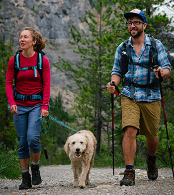 Two hikers walking with a dog on leash
